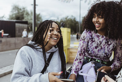 Female teenager female friends laughing with smart phone on footpath