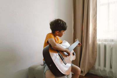 Cute boy learns to play the classical guitar in home. cozy home.