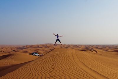 Man with arms outstretched jumping on desert against sky during sunset