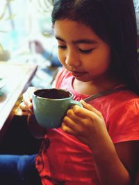 Girl holding coffee cup while sitting at cafe