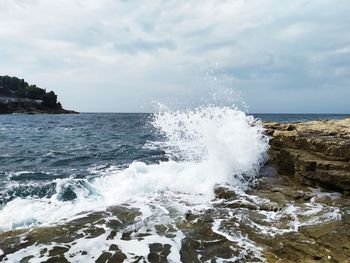 Sea waves splashing on shore against sky