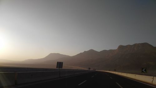 Road leading towards mountains against clear sky