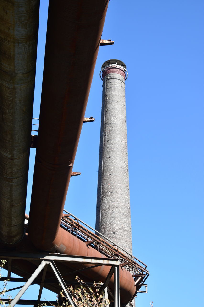 low angle view, architecture, built structure, sky, building exterior, factory, clear sky, nature, day, smoke stack, industry, architectural column, tall - high, no people, metal, tower, pipe - tube, outdoors, sunlight, blue, pollution