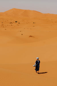 Man on sand dune in desert against sky