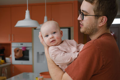 Daddy with baby girl in his hands cuddling on the kitchen at home, taking care of infant. father