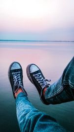 Low section of man relaxing on sea against sky