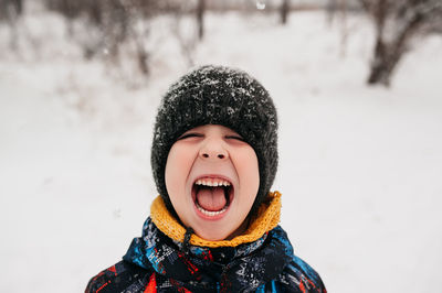 Preschool boy in warm hat a winter waterproof jacket close-up portrait catches snowflakes in tongues