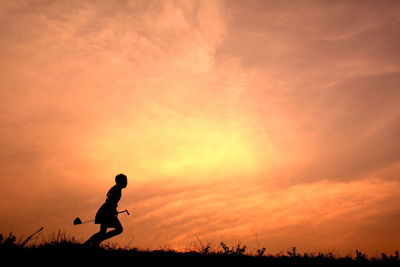 Silhouette person running on field against cloudy orange sky during sunset