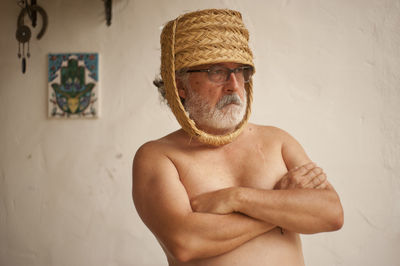 Portrait of shirtless man wearing hat standing against wall
