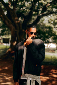 Young man wearing sunglasses standing against trees