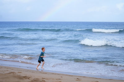 Young boy playing in the waves with a rainbow over the ocean on ka'anapali beach in hawaii. 