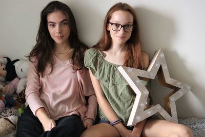 Portrait of sisters sitting against wall at home