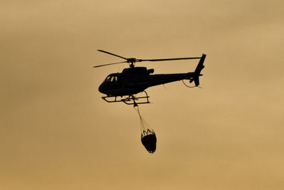 Low angle view of silhouette helicopter with parachute flying against sky during sunset