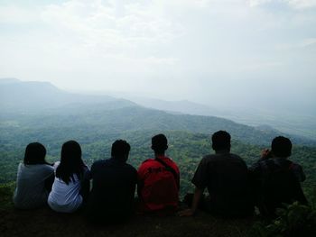 Rear view of friends sitting on hill against sky