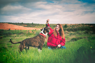 Smiling woman playing with dog sitting on land against sky