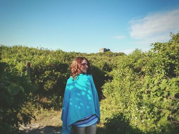 Woman standing by tree against blue sky