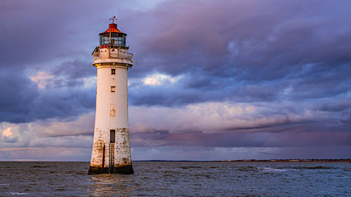 Lighthouse by sea against sky during sunset