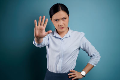 Portrait of young woman standing against blue background