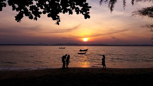 Silhouette people on beach against sky during sunset