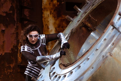 Strong woman in silver glasses and futuristic dress stands against the smoke in destroyed factory