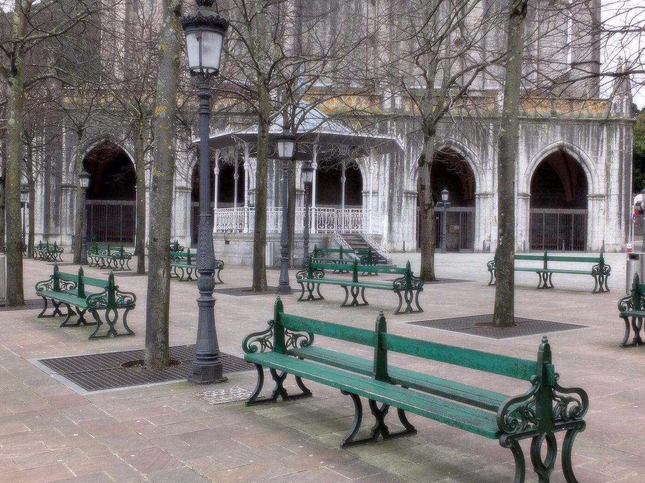 architecture, built structure, building exterior, tree, arch, bench, chair, cobblestone, day, building, shadow, architectural column, sunlight, city, entrance, empty, outdoors, facade, window, footpath