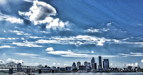 Scenic view of city by river against cloudy sky