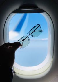 Low angle view of human hand against sky seen through window