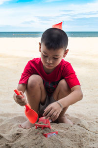 Boy crouching while playing with sand at beach