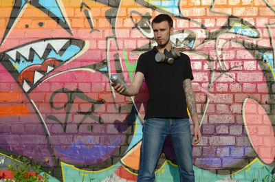 Full length of young man standing against graffiti wall