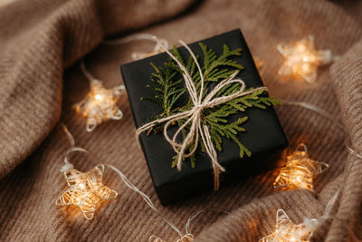 Christmas gift packed in black wrapping paper lying on soft woolen background. luminous garland