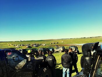 Rear view of people standing on field against clear sky