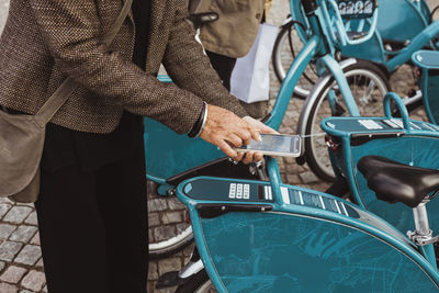 Midsection of senior woman scanning qr code of bicycle through smart phone at parking station