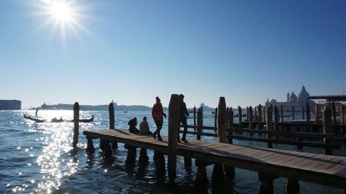 People on pier by grand canal against sky on sunny day in city