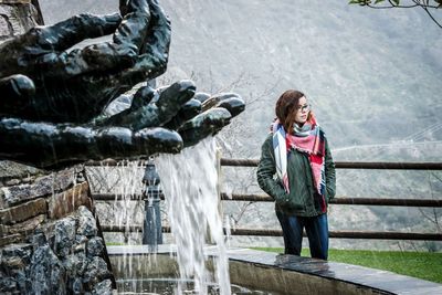 Young woman standing by fountain against railing during winter
