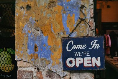 Close-up of open sign hanging on damaged wall