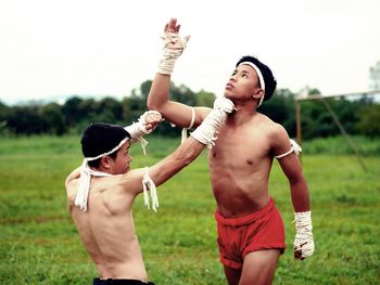 Shirtless male fighters practicing on grass against sky