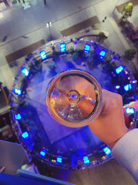 Close-up of hand holding glass against illuminated lights