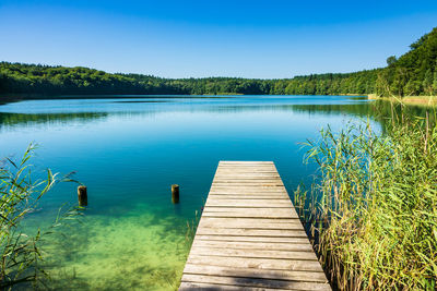 Pier over lake against clear blue sky