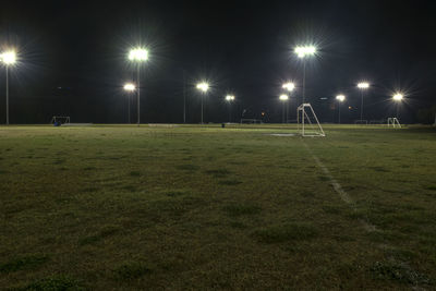 Illuminated lights on soccer field against sky at night