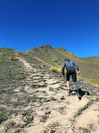 Rear view of disable man climbing mountain against clear blue sky