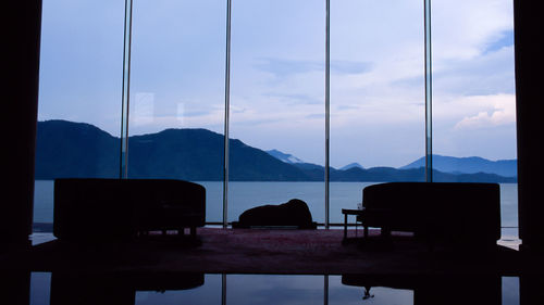 Silhouette chairs and tables against sky seen through window