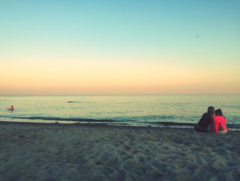 People sitting on beach against clear sky during sunset