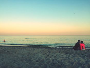 Rear view of mother with daughter sitting on shore at beach