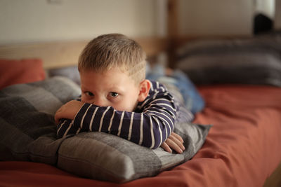 Thoughtful serious offended boy hugs a pillow on the couch, concept children's problems loneliness.