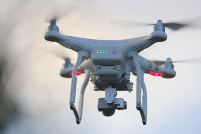  rear view of a white quadcopter drone with lights, against blue evening sky. motion blur propeller