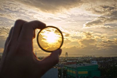 Close-up of hand holding lens against sky during sunset