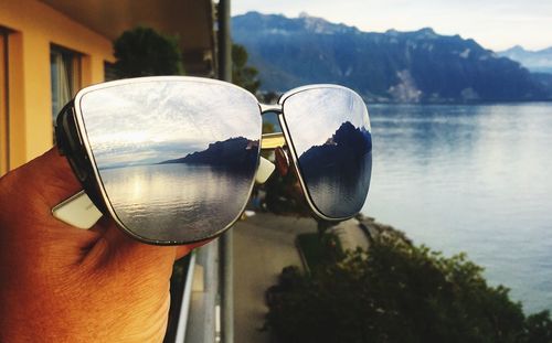 Close-up of hand holding sunglasses against sky