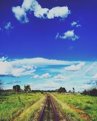 Road passing through field against cloudy sky