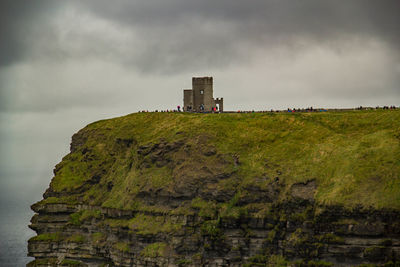 Low angle view of cliff against cloudy sky