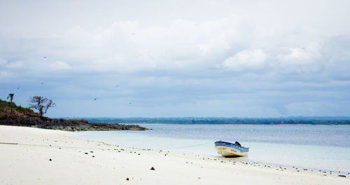 Lone boat on calm beach against clouds